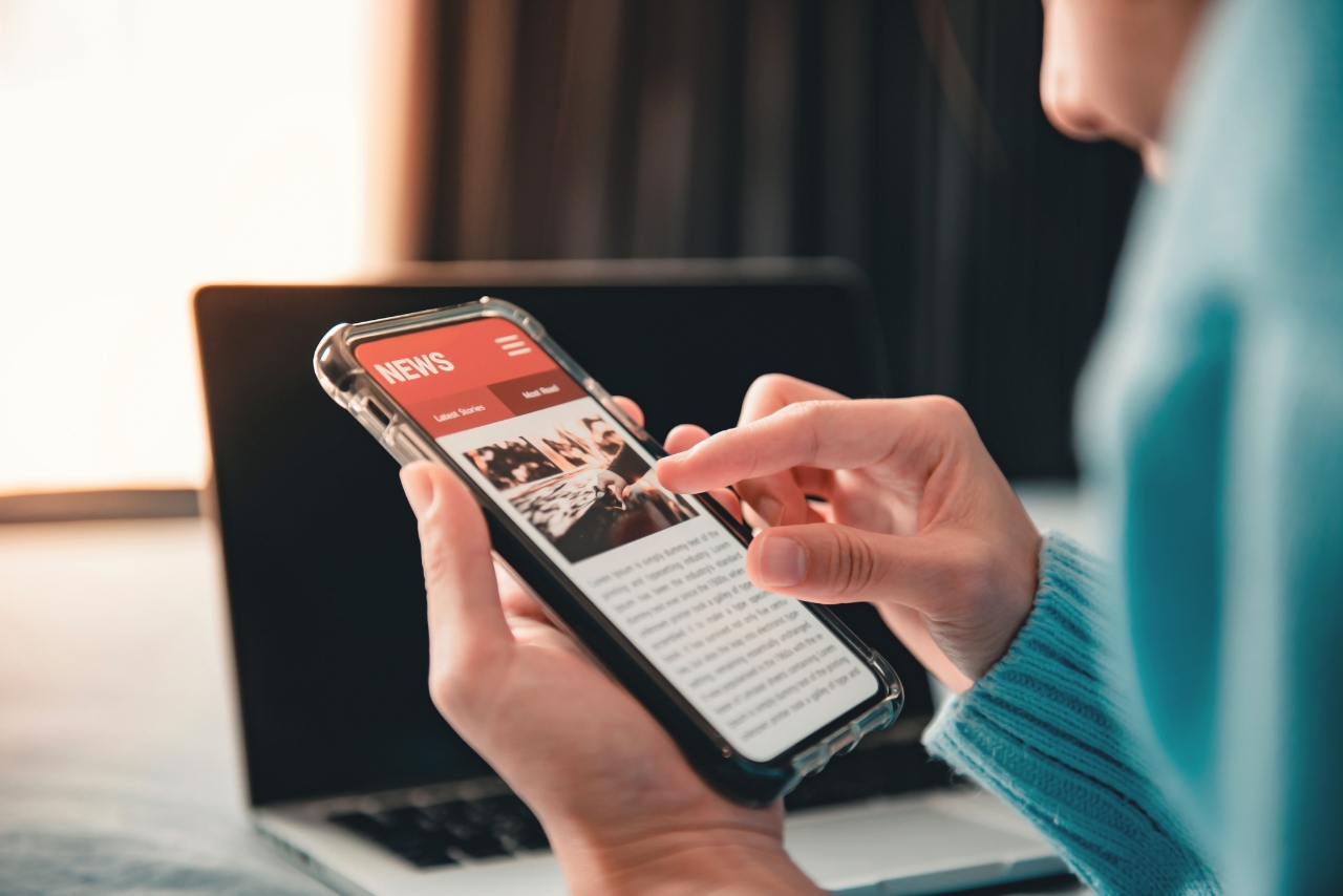 1295073326 Online news on a smartphone. (Mockup website). Woman reading news or articles in a mobile phone screen application at home. Newspaper and portal on internet.